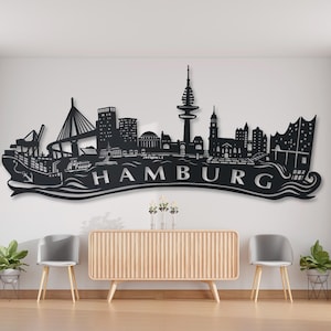 May include: Black metal wall art depicting the Hamburg skyline with the text "HAMBURG" in a white font. The art is mounted on a white wall in a modern living room setting.