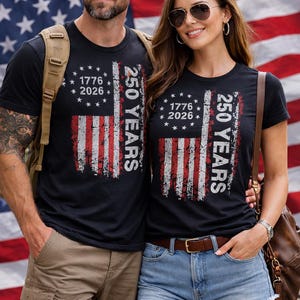 Puede incluir: Camisetas negras con un dise&ntilde;o desgastado de la bandera estadounidense. Las camisetas presentan el texto "1776 2026" y "250 YEARS". El fondo es una bandera estadounidense.