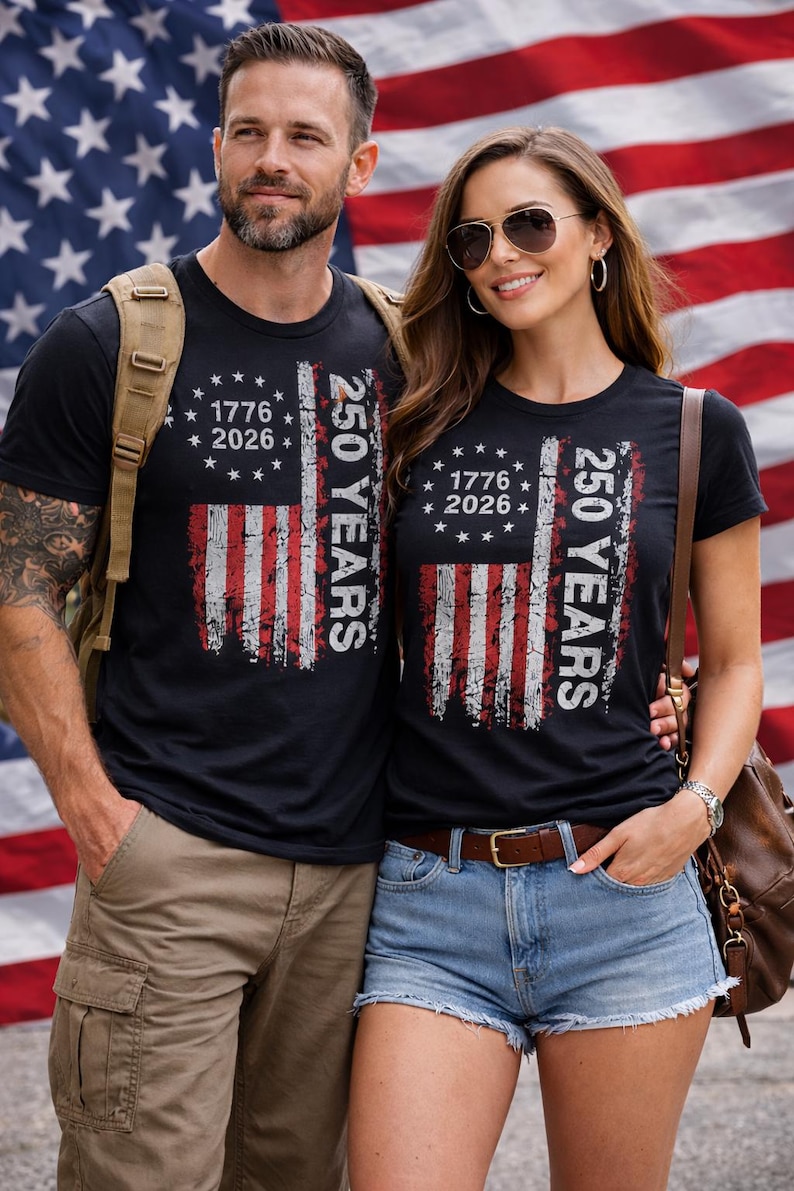 Puede incluir: Camisetas negras con un dise&ntilde;o desgastado de la bandera estadounidense. Las camisetas presentan el texto "1776 2026" y "250 YEARS". El fondo es una bandera estadounidense.