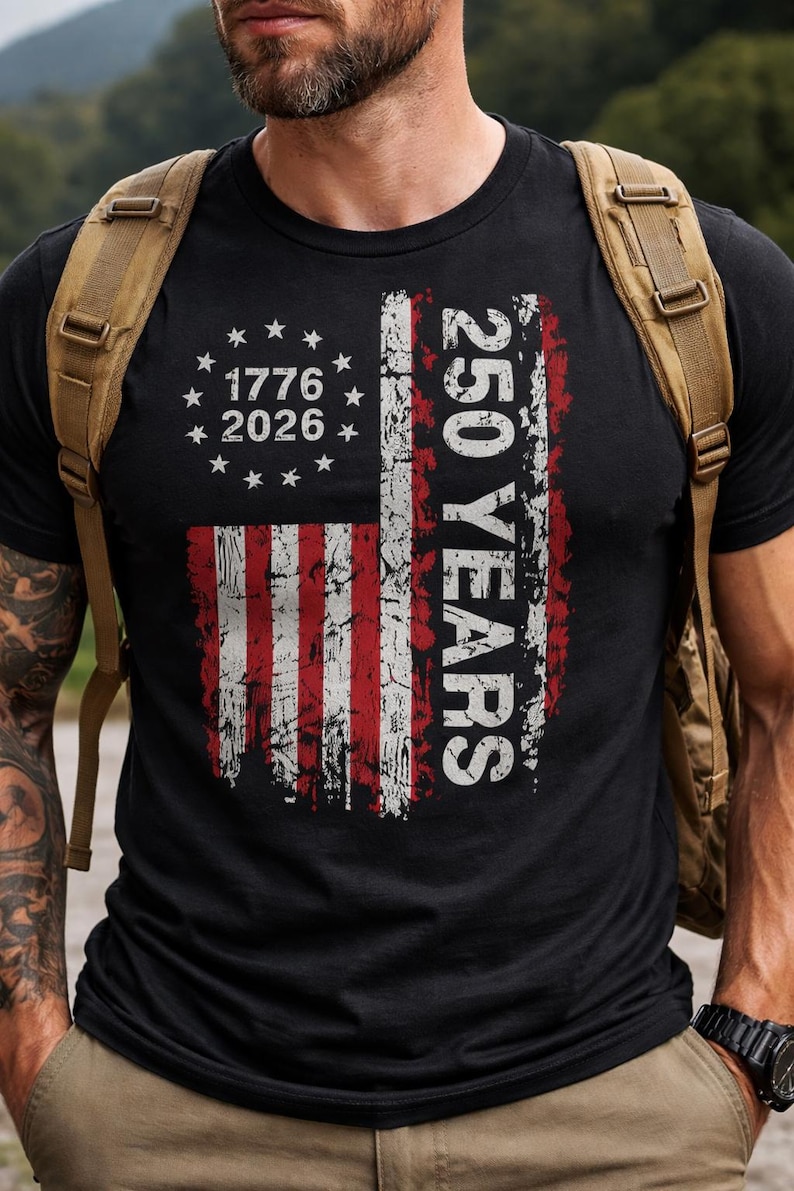 Puede incluir: Camiseta negra con un dise&ntilde;o desgastado de la bandera estadounidense con rayas rojas y blancas y estrellas. La camiseta incluye el texto "1776 2026" y "250 YEARS" en blanco, celebrando un hito hist&oacute;rico.
