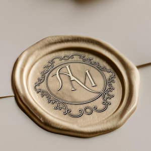 以下が含まれることがあります： クリーム色の封筒の上に、イニシャル「AM」が楕円のフレームに入った金のワックスシール。 シールは装飾的なデザインで、わずかに浮き上がっています。 下部には「DESIGN MOCKUPS ARE NOT INCLUDED」という文字があります。