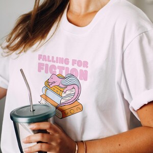 A cozy fall aesthetic t-shirt mockup featuring a retro hand drawn illustration of an open book with autumn leaves and the phrase “Cozy Fall Girl Book Club.” Perfect for book lovers, fall vibes, sublimation design, retro stickers, or autumn reading apparel. High resolution PNG design for book club fashion, Thanksgiving outfits, and cozy girl autumn style.