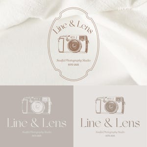 Può includere: Un design del logo con un'illustrazione di fotocamera vintage all'interno di una cornice ovale. Il testo "Line & Lens" e "Soulful Photography Studio ESTD 2025" sono visualizzati in un carattere serif. Il design è in tonalità marroni.