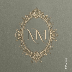 May include: A grey card featuring an oval, gold-coloured frame with intricate floral and scrollwork. The frame contains the intertwined letters "NM". The text "WOOF studio" is in the bottom right corner. The design has a classic, elegant feel.