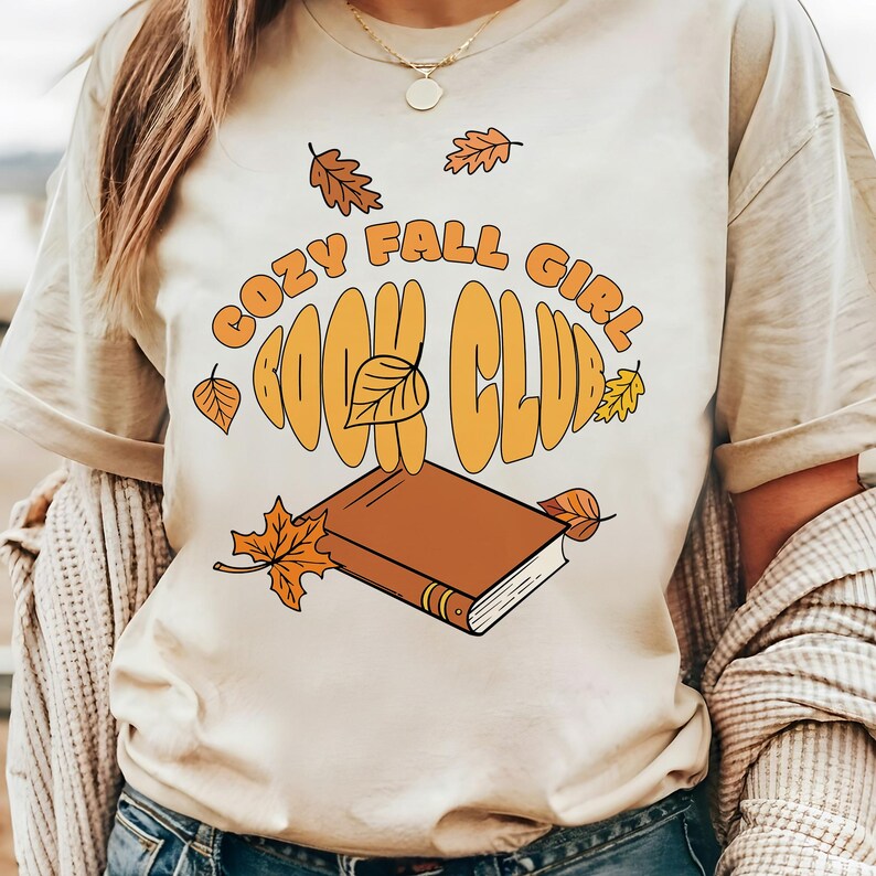 A cozy fall aesthetic t-shirt mockup featuring a retro hand drawn illustration of an open book with autumn leaves and the phrase “Cozy Fall Girl Book Club.” Perfect for book lovers, fall vibes, sublimation design, retro stickers, or autumn reading apparel. High resolution PNG design for book club fashion, Thanksgiving outfits, and cozy girl autumn style.