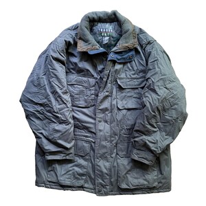May include: A dark gray Trader Bay jacket with a corduroy collar and multiple front pockets. The jacket has a button and snap closure and a quilted lining. The text "TRADER BAY" is visible on the collar.