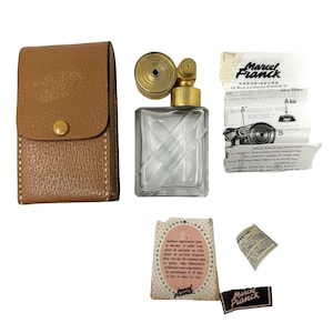 Puede incluir: Un atomizador de perfume Marcel Franck vintage con un frasco de vidrio transparente, un pulverizador de metal dorado y un estuche de cuero marrón. Incluye insertos de papel impreso y una pequeña etiqueta.