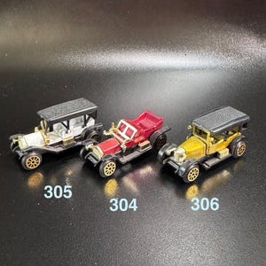 Może przedstawiać: Trzy zabytkowe samochodziki, biały samochód z czarnymi ozdobami, czerwony samochód ze złotymi ozdobami i złoty samochód z czarnymi ozdobami. Samochody są ponumerowane 305, 304 i 306.