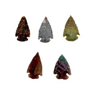 May include: Five antique arrowheads in various colors, including brown, gray, and green, are displayed against a white background. Each arrowhead has a distinct shape and texture, showcasing the craftsmanship of ancient tools.