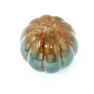 May include: A round, ceramic pumpkin-shaped decorative object with a glossy finish. The surface features a blend of warm brown tones at the top that transition into deep teal and blue hues toward the base, with vertical ridges defining the shape.