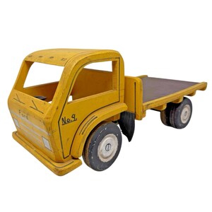 May include: A vintage wooden toy truck painted yellow with black tires and a flatbed. The truck has the word "Ford" and the number "No. 9" painted on the side. The toy truck is a classic design.
