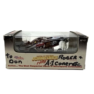 May include: A black and red John Force 1996 A-1 Concrete drag racing car in a clear display case. The car has "Castrol GTX" branding. The box is labeled "To Don" and "Action... The Most Respected Name In Motorsports Collectables."
