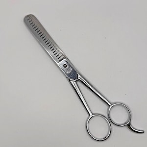 Könnte beinhalten: Silberne Friseurscheren mit einer gezahnten Klinge und zwei Ringen.