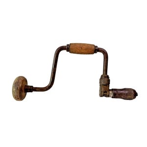 Puede incluir: Un taladro de mano vintage con mango de madera y partes metálicas. El taladro está oxidado y tiene un acabado desgastado.