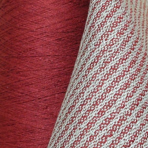 May include: Close-up of a spool of red yarn next to a piece of fabric with a white and red striped pattern.