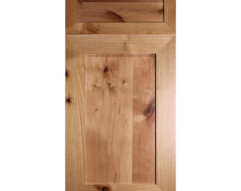 May include: A light wood cabinet door with a raised panel and a single drawer above. The door has a rustic, knotty wood grain.