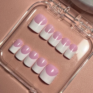 May include: A set of press-on nails with a French manicure design. Each nail has a white base with a rounded, pale pink tip. The nails are arranged in a clear plastic case, ready for application.
