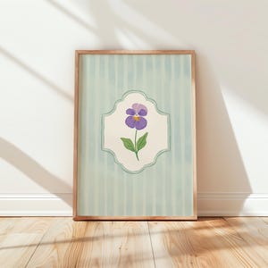May include: A framed print with a light blue and white striped background. A purple pansy flower is featured in a decorative white frame.