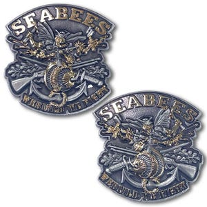 May include: Two metal SEABEES emblems with a detailed design. The emblems feature the word "SEABEES" in gold lettering, along with crossed rifles, an anchor, and the text "WE BUILD, WE FIGHT". The design incorporates gold and silver tones.