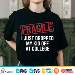 May include: A black short-sleeve t-shirt featuring a red rectangular stamp graphic with the word FRAGILE in distressed lettering. Below the stamp, the white text reads I JUST DROPPED MY KID OFF AT COLLEGE in a bold, sans-serif font style.