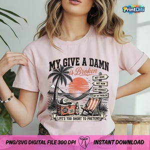 Pode incluir: Uma t-shirt rosa claro com um gr&aacute;fico de praia que inclui uma palmeira, uma rede, uma geleira e uma cadeira de praia. O texto diz: MY GIVE A DAMN is Broken, NOT HERE, NOT NOW, NOT WORRIED, NOT MY PROBLEM, LIFE'S TOO SHORT TO PRETEND.