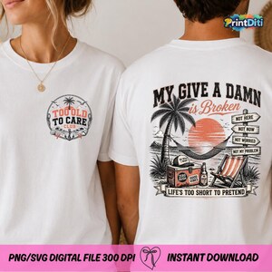 Pode incluir: Uma t-shirt branca com um pequeno log&oacute;tipo circular no peito que diz Too Old To Care Club. As costas apresentam uma cena de praia tropical com uma rede, palmeira, geleira e cadeira, com o texto My Give A Damn Is Broken.