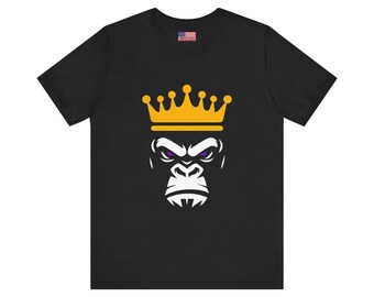 May include: Black t-shirt featuring a graphic of a gorilla wearing a gold crown. The gorilla's face is white with purple eyes. The shirt has a small American flag on the upper chest.