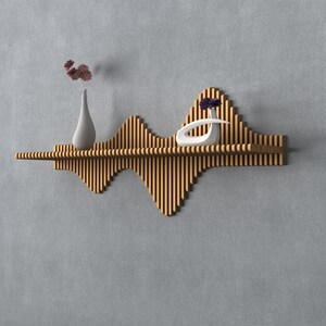 May include: A modern wooden shelf with a unique wave-like design. The shelf holds a white vase with dried flowers, and a white decorative sculpture. The shelf is mounted on a gray wall, with a tall vase on either side.