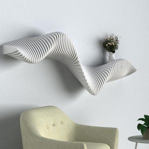 Può includere: Mensola a parete bianca con un design ondulato e organico. La mensola è vuota, tranne che per un piccolo vaso con fiori bianchi. Una poltrona giallo chiaro è in primo piano.