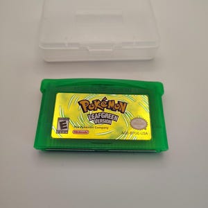 May include: A translucent green Game Boy Advance video game cartridge for Pokémon LeafGreen Version with a gold holographic label featuring the game title, the Nintendo logo, an ESRB E rating, and the product code AGB-BPGE-USA, with a clear plastic case.