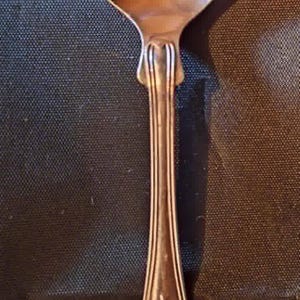 May include: A silver spoon with an ornate handle and a rounded bowl. The handle features detailed floral and scrollwork designs. The spoon is likely vintage or antique, and is made of a shiny metal.