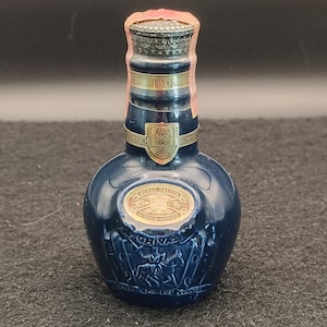 K&ouml;nnte beinhalten: Kleine, dunkelblaue Royal Salute Scotch Whisky Flasche. Die Flasche hat goldfarbene Schriftz&uuml;ge und ein goldenes Emblem. Die Flasche ist 50 ml und 80 Proof. Die Flasche hat ein dekoratives Design eines Pferdes und Reiters.