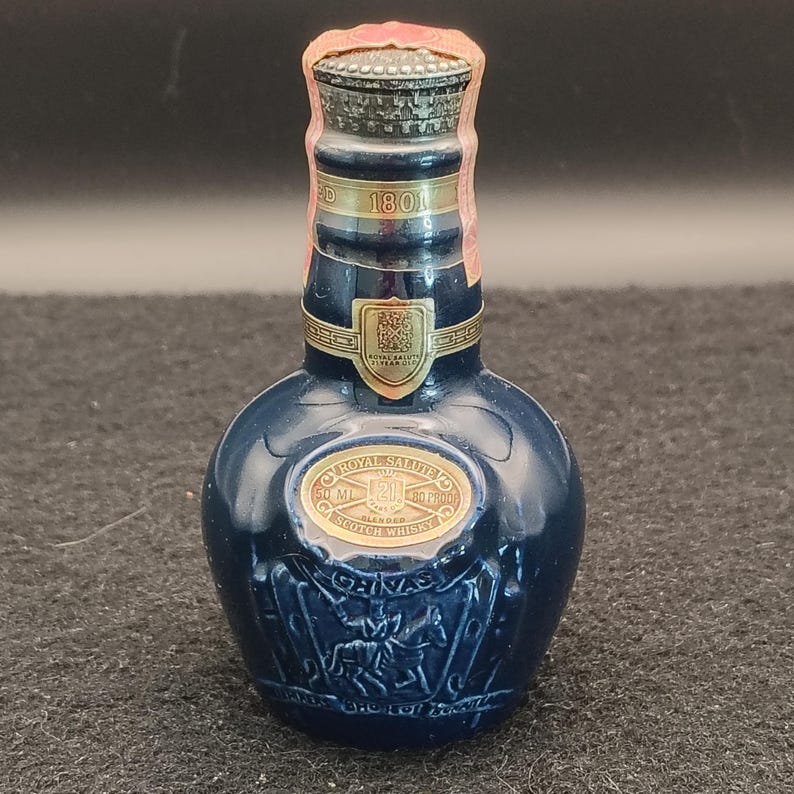 K&ouml;nnte beinhalten: Kleine, dunkelblaue Royal Salute Scotch Whisky Flasche. Die Flasche hat goldfarbene Schriftz&uuml;ge und ein goldenes Emblem. Die Flasche ist 50 ml und 80 Proof. Die Flasche hat ein dekoratives Design eines Pferdes und Reiters.