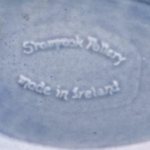 May include: Close-up of a light blue ceramic surface with the embossed text "Shamrock Pottery" and "Made in Ireland". The text is in a white, stylized font.