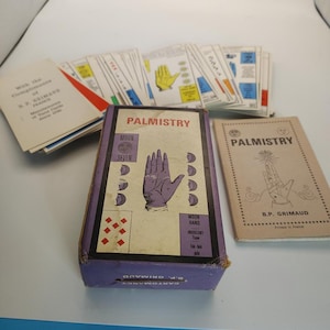 May include: A vintage palmistry card deck set featuring a purple box with a hand illustration, the text PALMISTRY, MOON, SEVEN, MOON HAND, INDOLENT Type, and a diamond pattern. Includes a tan instruction booklet and a stack of illustrated cards.