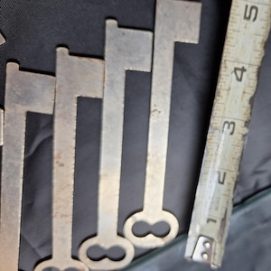 May include: Five silver skeleton keys with a double-looped end. The keys are arranged in a row, with the largest key at the top and the smallest key at the bottom.