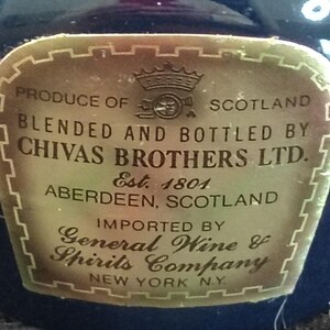 K&ouml;nnte beinhalten: Nahaufnahme eines goldenen Etiketts einer Flasche Chivas Brothers Ltd. Scotch Whisky. Das Etikett hat einen dekorativen Rand und Text, darunter "Produkt aus Schottland", "Gemischt und abgef&uuml;llt von" und "Est. 1801."
