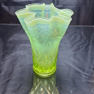 May include: A green glass vase with a ruffled top and a diamond pattern. The vase is made of uranium glass and glows under a black light.