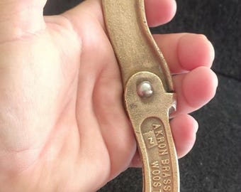 Puede incluir: Una llave de manguera contra incendios de latón vintage. La herramienta curva tiene un gancho en un extremo y un mango con el texto "AKRON BRASS MFG COMPANY INC WOOSER OHIO". También son visibles el número 6 y la letra Z.