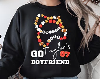 Könnte beinhalten: Schwarzer Pullover mit einem weißen Grafikdesign, das ein Herz aus Würfeln, Fußbällen und Herzen zeigt. Der Text "Go Taylor's 87 Boyfriend" befindet sich unter dem Herzen.