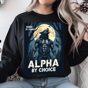 May include: Black sweatshirt with a graphic of a werewolf in a forest with a full moon. The text "Human by Chance, Alpha by Choice" is printed on the sweatshirt.