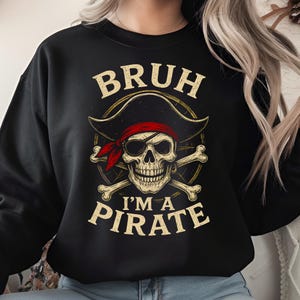 May include: Black sweatshirt featuring a pirate skull design with a red bandana, eye patch, and crossed bones. The text "BRUH I'M A PIRATE" is printed above and below the skull in a distressed font. The design is centered on the chest.