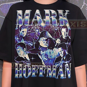 Könnte beinhalten: Schwarzes T-Shirt mit einem Grafikdesign mit dem Namen "MARK HOFFMAN" in einer stilisierten Schriftart. Das Design enthält Bilder von Männern und Blitzen und erzeugt eine Vintage-Ästhetik.