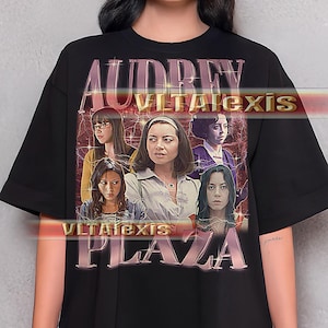 May include: Black t-shirt featuring a graphic of Audrey Plaza with the text "AUDREY PLAZA" in a vintage style. The shirt has a crew neck and short sleeves. The graphic includes multiple images of Audrey Plaza.