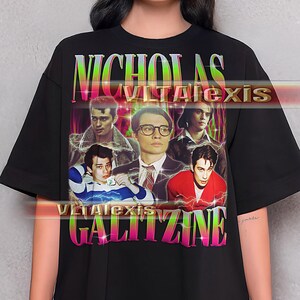 May include: Black t-shirt featuring a graphic of Nicholas Galitzine with the text "NICHOLAS GALITZINE" in a colorful, gradient font. The design includes multiple images of the actor. The shirt is a casual, oversized fit.