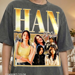 Könnte beinhalten: Dunkelgraues Comfort Color T-Shirt mit einer Grafik einer Frau und dem goldenen Text "HAN So Hee". Das Shirt hat einen Vintage-Look, mit den Wörtern "COMFORT COLOR" und "PEPPER" unten gedruckt.