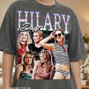 Könnte beinhalten: Dunkelgraues Comfort Color Pepper T-Shirt mit einem Vintage-Grafik von Hilary Duff. Die Grafik zeigt den Namen "Hilary Duff" in Lila und Weiß sowie mehrere Bilder der Prominenten.