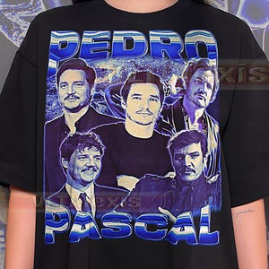 May include: Black t-shirt with a blue graphic featuring multiple images of Pedro Pascal and the name "PEDRO PASCAL" in a retro font. The design has a vintage aesthetic.