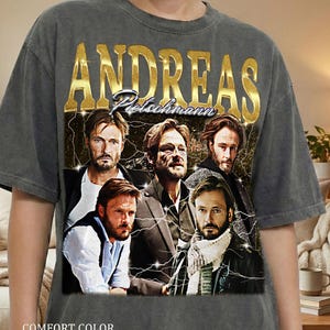 Op de afbeelding: Donkergrijs Comfort Color Pepper T-shirt met een vintage afbeelding van Andreas Pietschmann. Het ontwerp bevat gouden tekst van zijn naam en meerdere afbeeldingen van de acteur met bliksemaccenten.