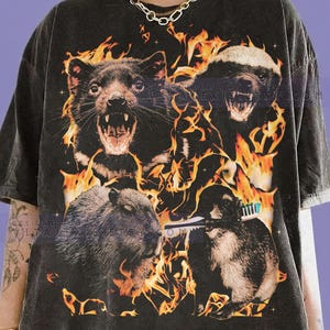 Könnte beinhalten: Dunkelgraues T-Shirt mit einem Aufdruck von vier Tieren mit Flammen. Die Tiere sind ein Tasmanischer Teufel, ein Honigdachs, ein Biber und ein Waschbär mit einer Zahnbürste. Der Text "COMFORT COLORS" und "GRAPHITE" befindet sich unten.